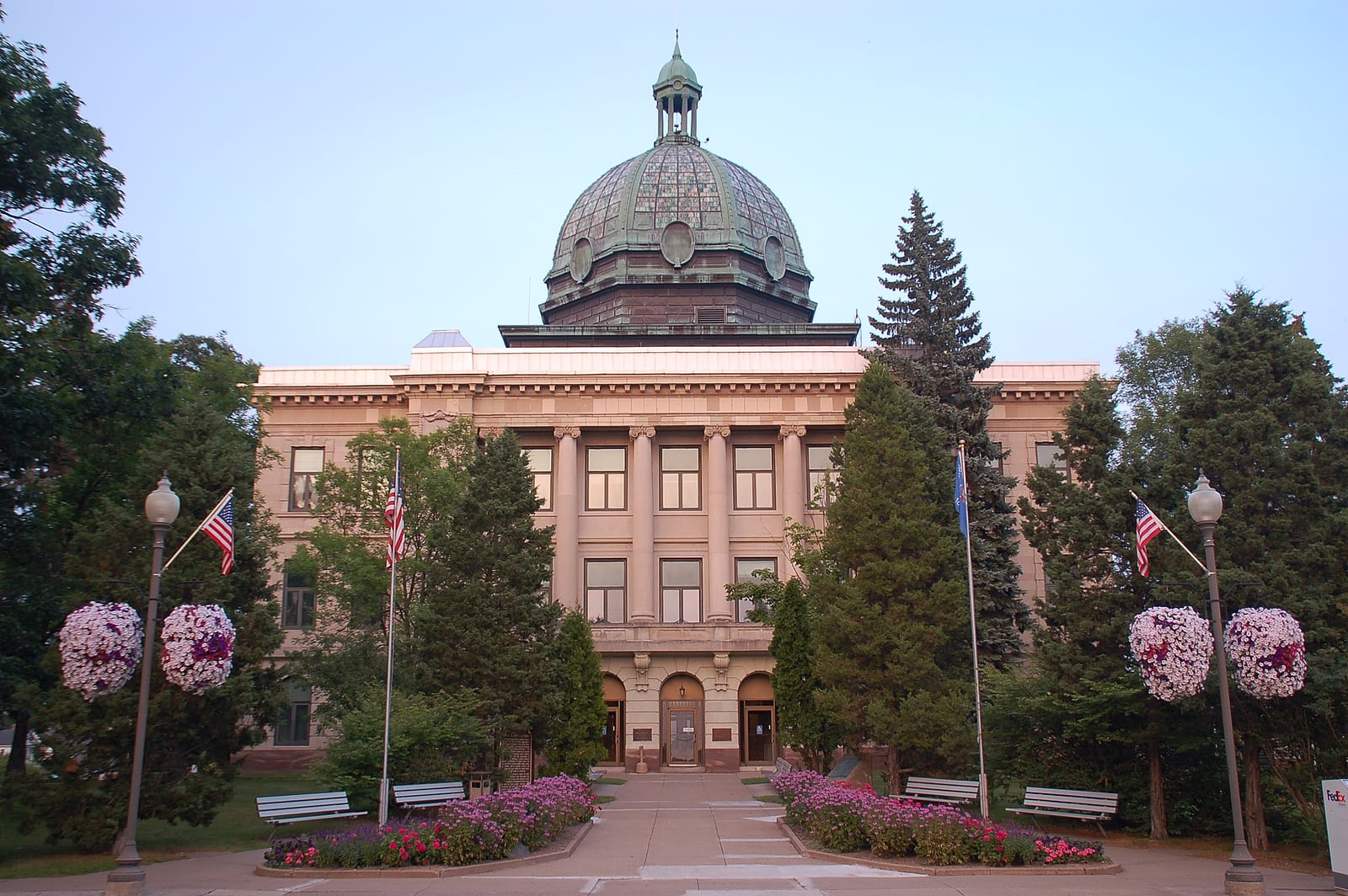 Front view of a grand historic courthouse with a domed roof, surrounded by trees and flower beds