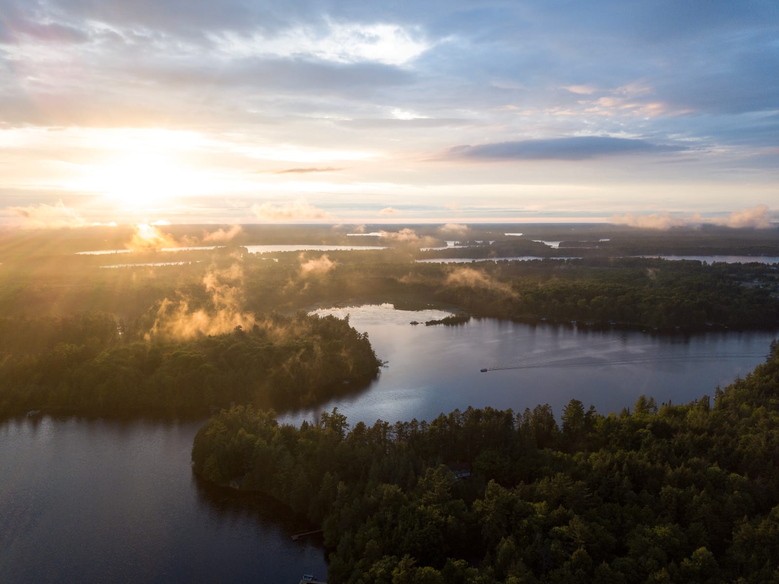 Aerial view of lush forests and winding rivers in Oneida County, Wisconsin, with a sunrise casting a golden glow over the scenery