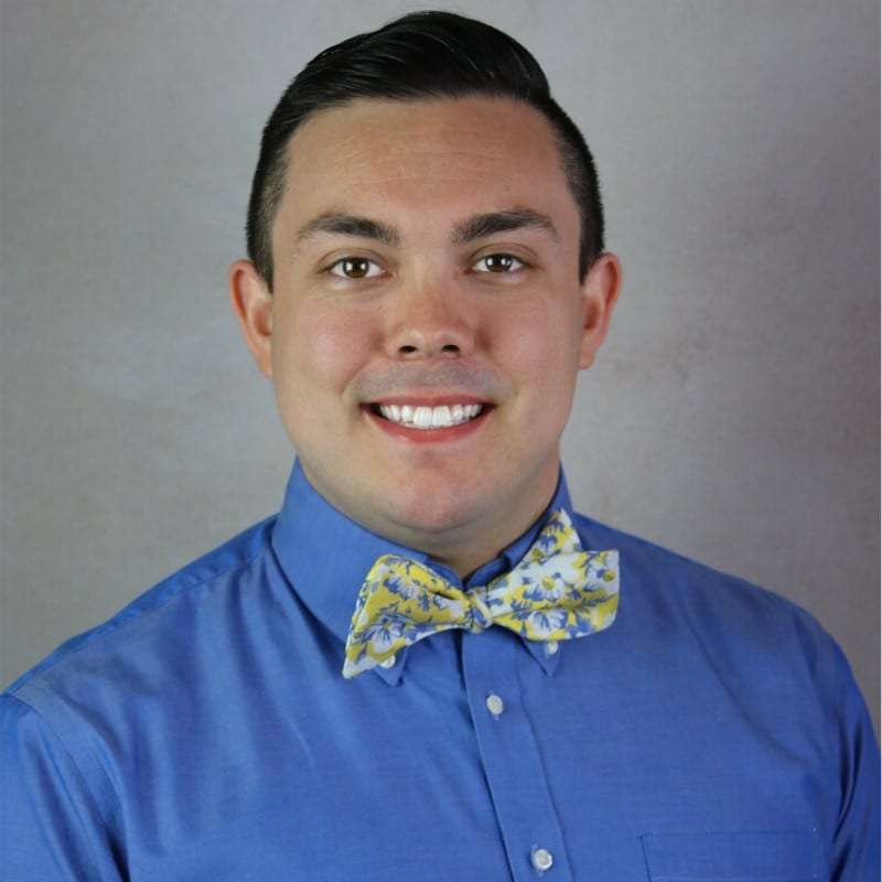 Portrait of a person in a blue shirt and patterned bow tie against a gray background