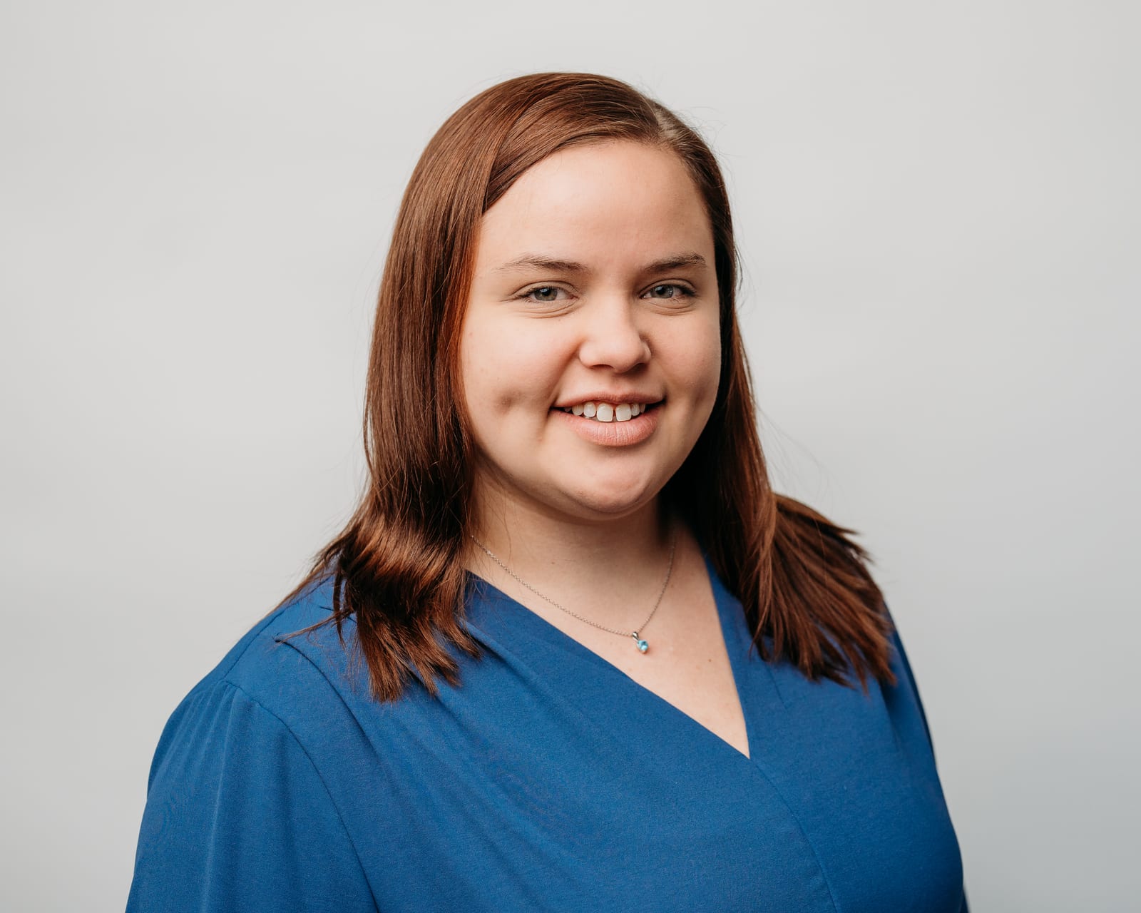 Portrait of a person with brown hair wearing a blue shirt against a light background