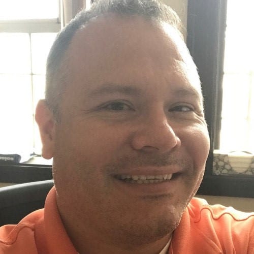 Close-up portrait of a person smiling indoors, wearing a casual orange shirt