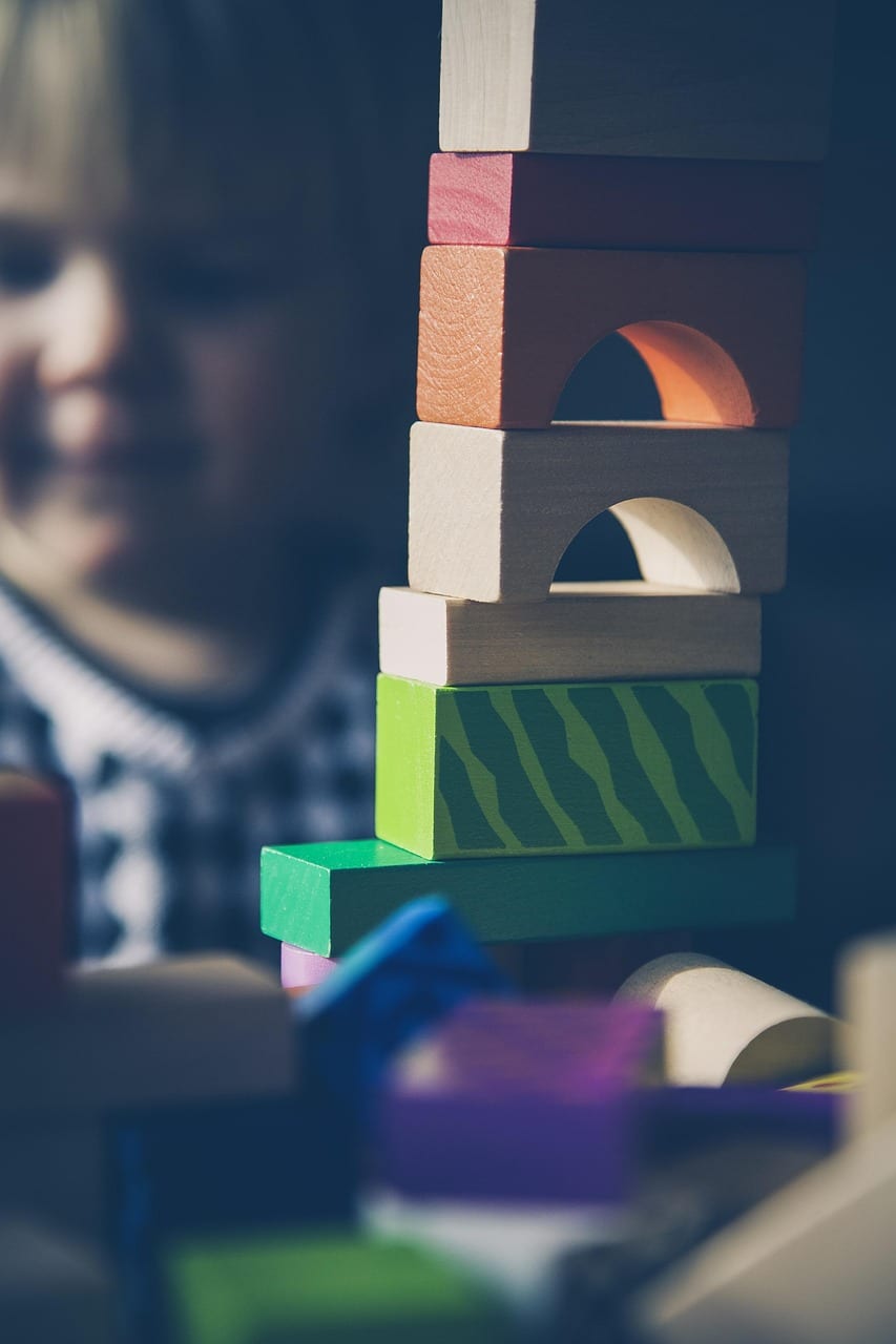 A child playing with colorful building blocks at a daycare, focusing on a tower of blocks in vibrant hues.