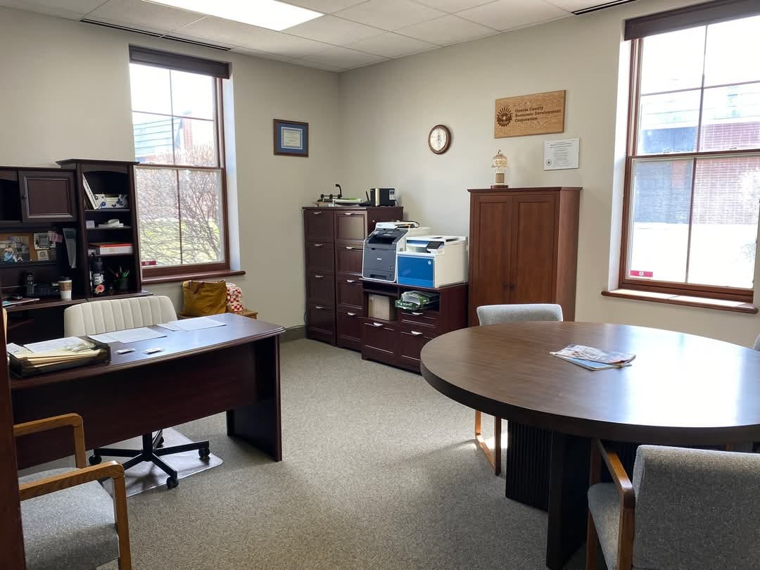 A well-lit, organized office space with desks, chairs, filing cabinets, and large windows viewed during the day.