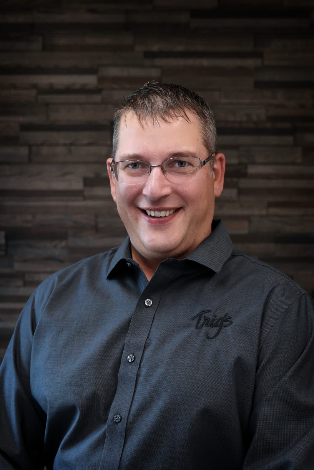 Smiling individual in formal attire against a wooden background