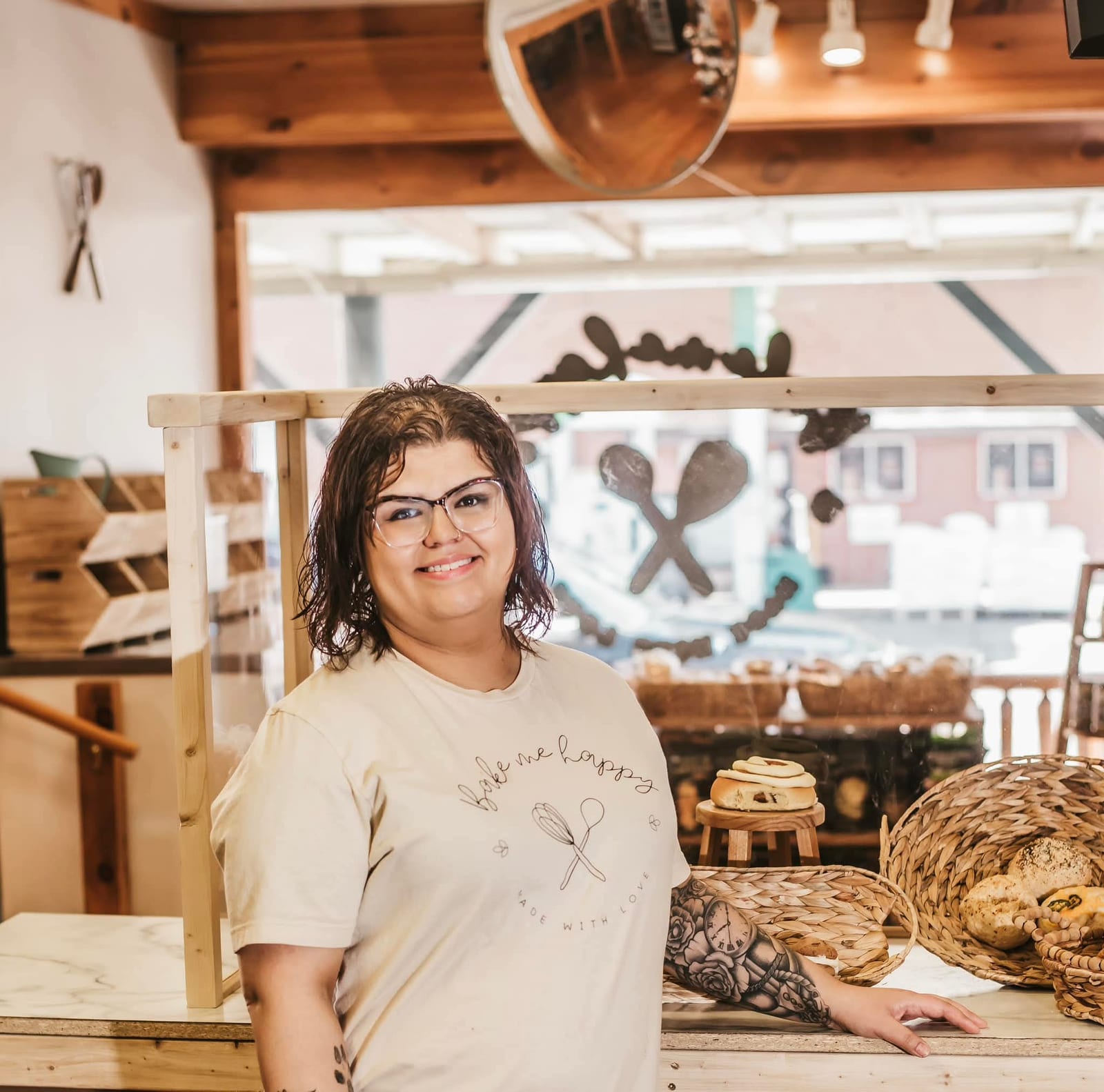 A smiling woman stands in front of a display of fresh baked goods inside a cozy bakery, representing small business growth in Oneida County, Wisconsin.