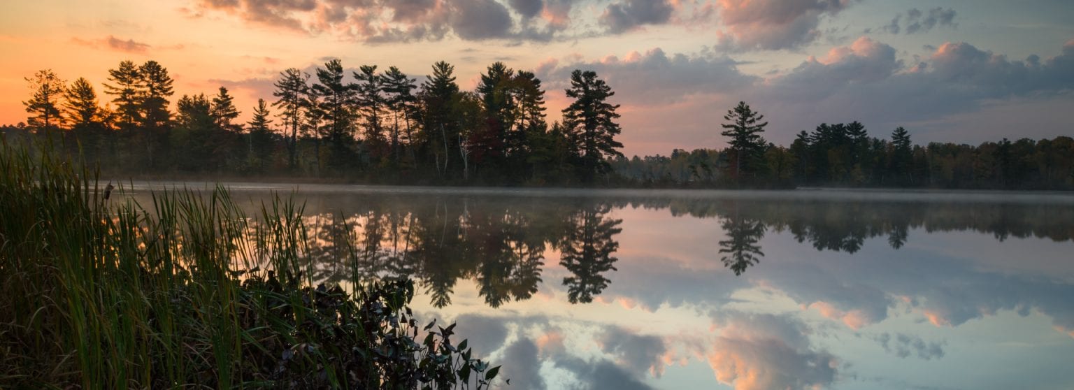 Scenic view of a calm lake reflecting a forest and a colorful sunset sky in Oneida County, Wisconsin