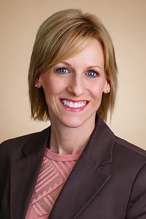 Portrait of a person wearing a brown blazer, smiling with a light brown background