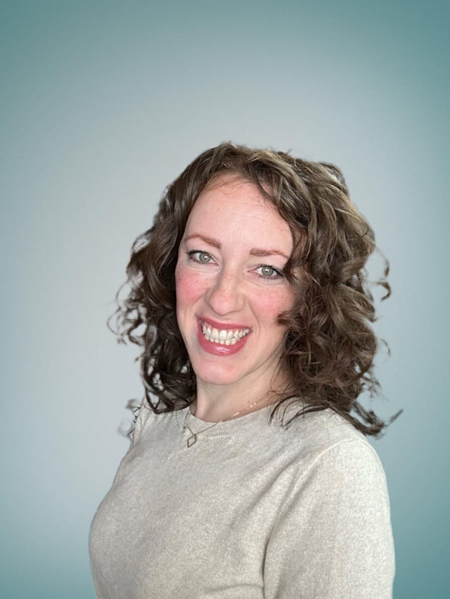 Portrait of a smiling person with curly hair against a gray background
