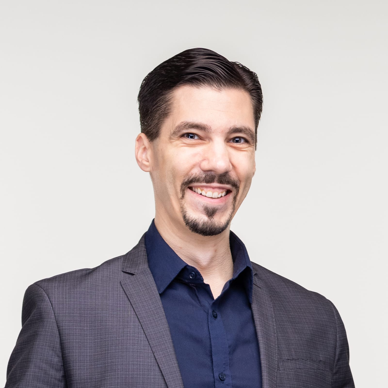 Smiling man in a dark blazer and navy shirt, posing for a professional headshot with a neutral light background.