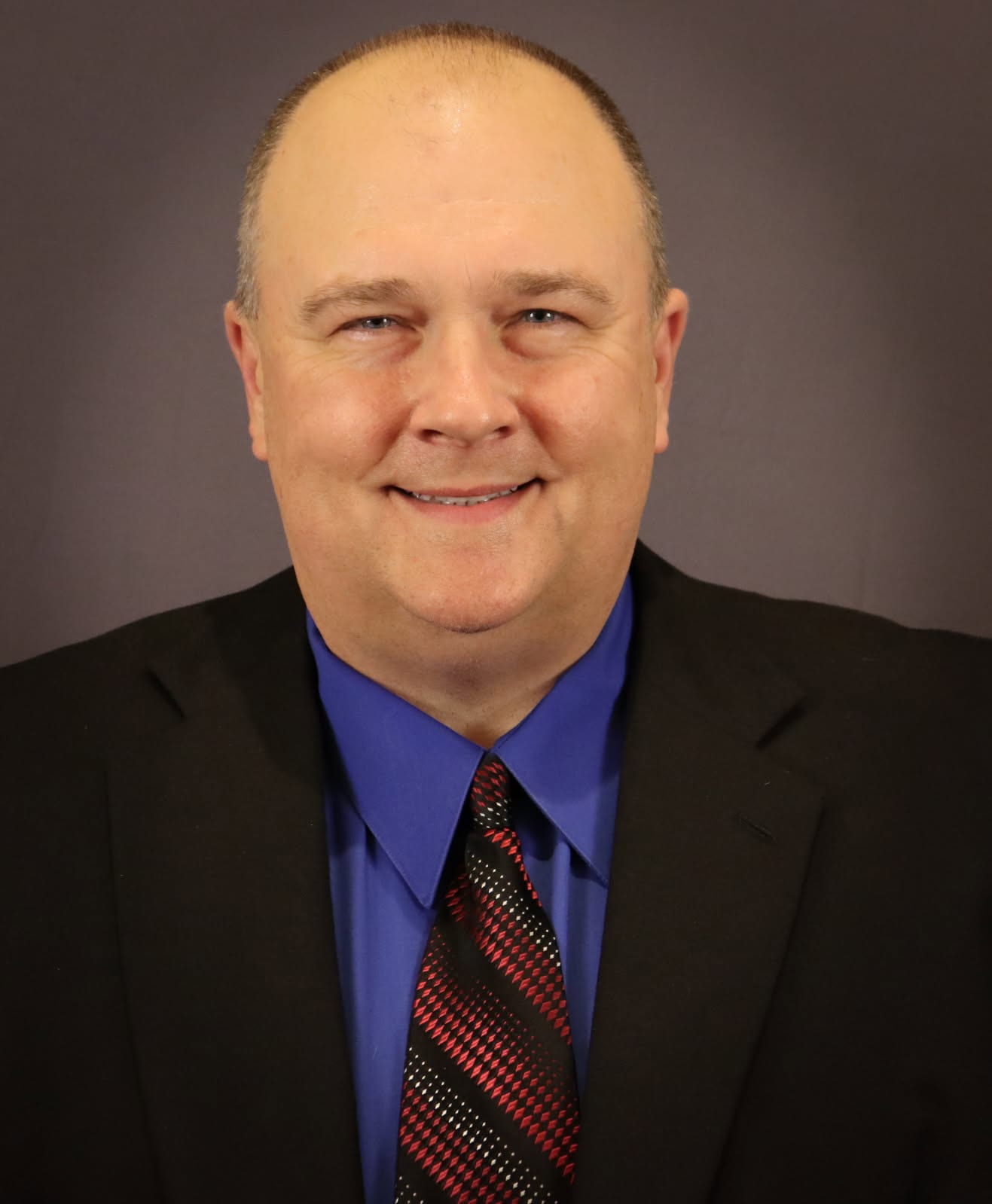 Professional headshot of a smiling individual in a suit with a brown and blue background