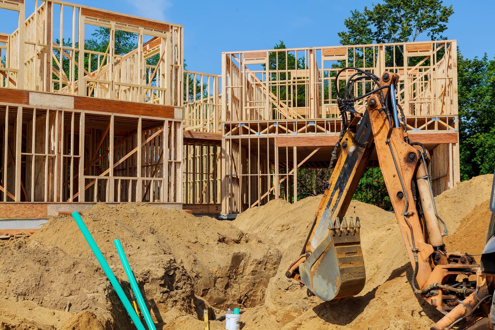 Unfinished wooden house under construction with an excavator in front