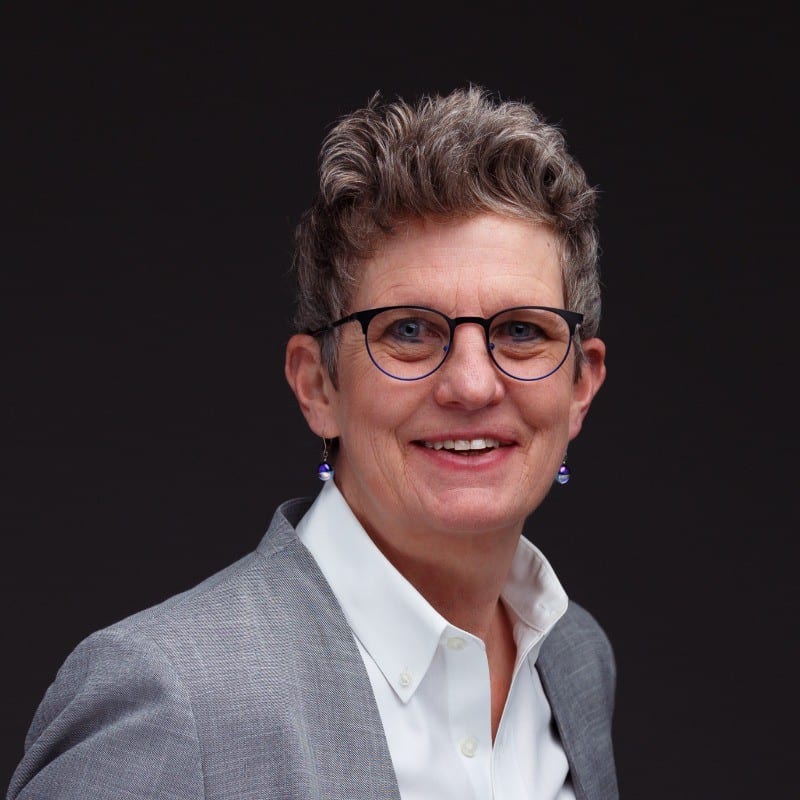 Square portrait of a person wearing glasses and a suit jacket against a dark background
