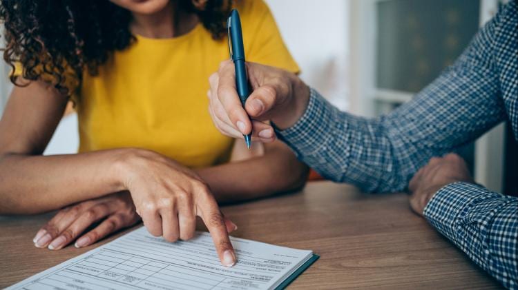 Close-up of two hands, one pointing and the other holding a pen over documents on a table