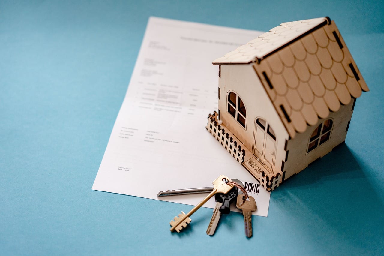 Model house and keys on top of loan documents against a blue background